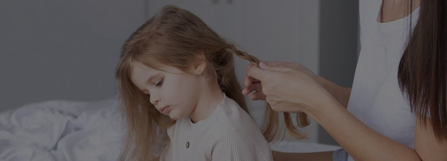 Gros plan sur des mains qui tressent les cheveux d’un enfant – symbole de l’importance du soin et de l’attention