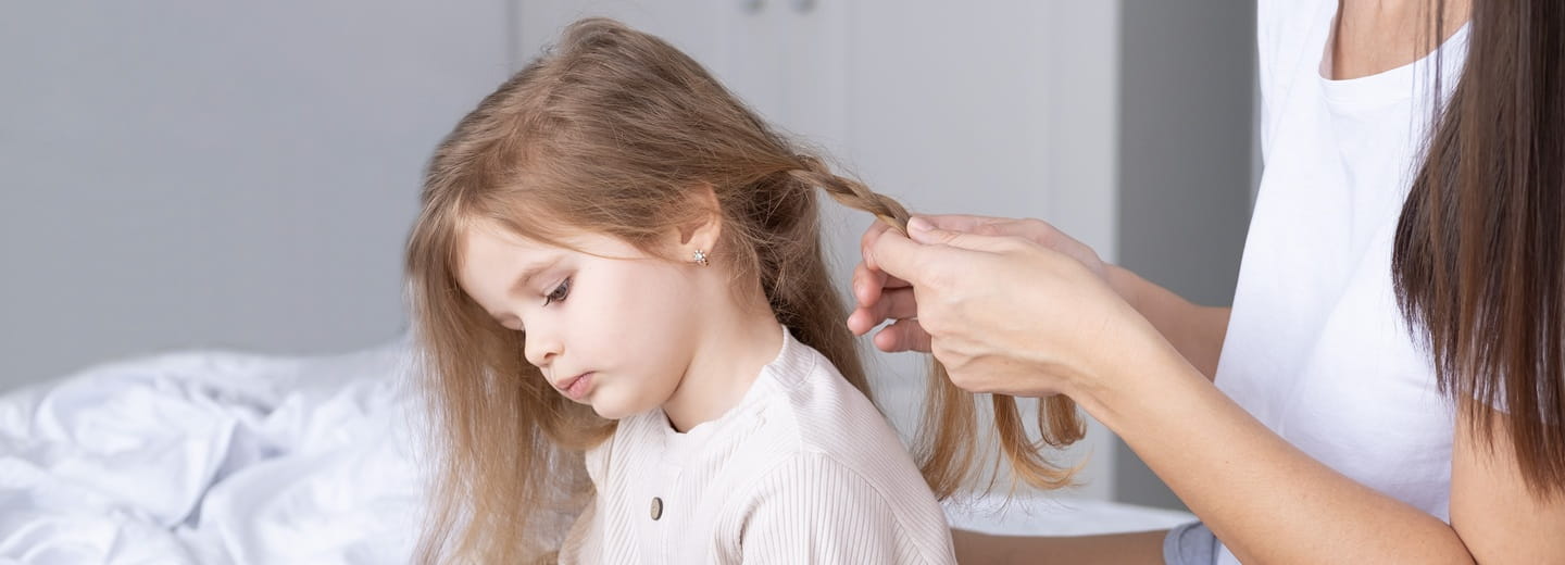 Gros plan sur des mains qui tressent les cheveux d’un enfant – symbole de l’importance du soin et de l’attention