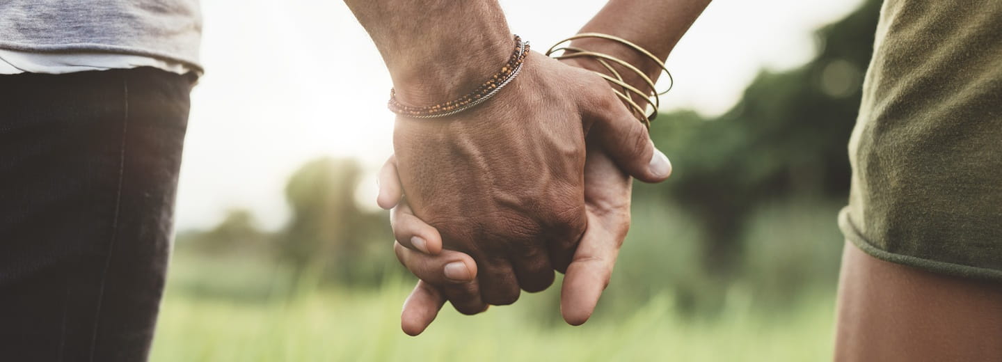 Deux mains qui s’entrelacent délicatement, sur un fond neutre – symbole d’attention et de contact.