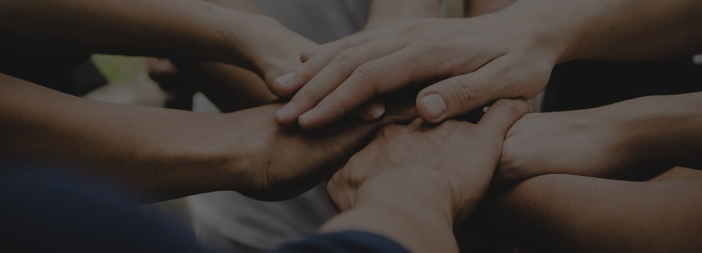 Un gruppo di persone unisce le proprie mani in segno di supporto – simbolo di protezione e comunità.