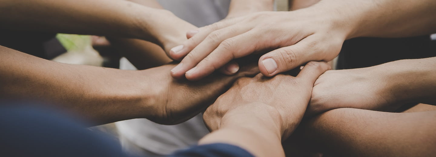 Un gruppo di persone unisce le proprie mani in segno di supporto – simbolo di protezione e comunità.