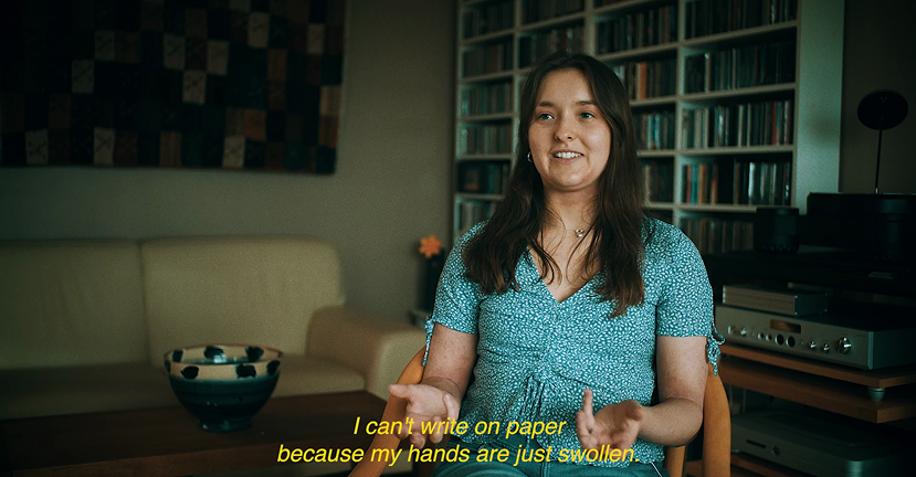Photograph of a Emma, real patient with Chronic Hand Eczema, smiling in front of a bookcase.