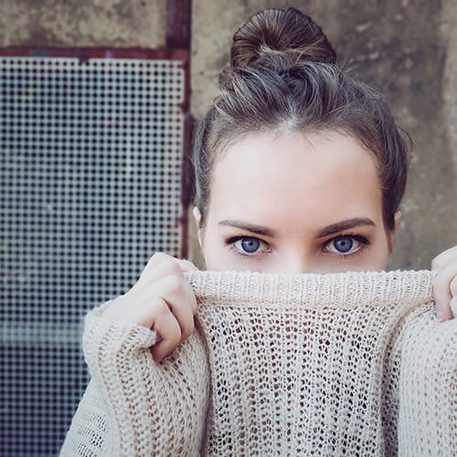 Dark haired woman in gray turtleneck covering part of her face