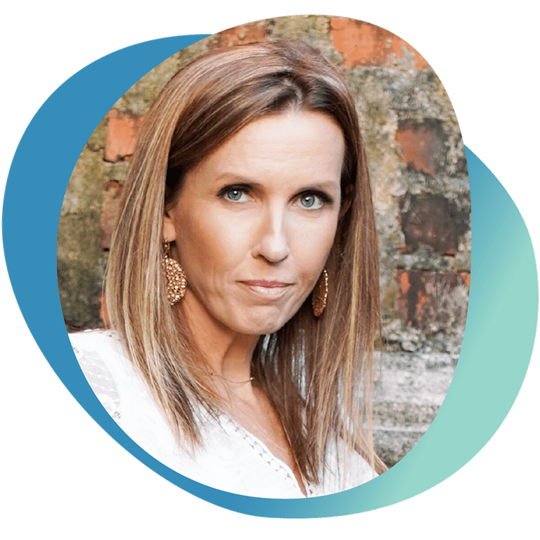 Portrait of Heather with long straight hair and gold earrings, standing in front of a brick wall