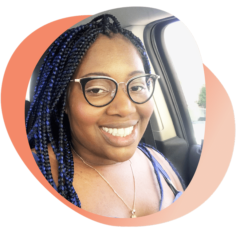 Portrait of Mary smiling while seated in a car, wearing glasses and a necklace